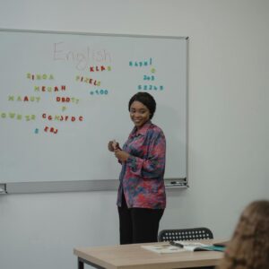 A female teacher explaining an English lesson to students in a classroom with a whiteboard.