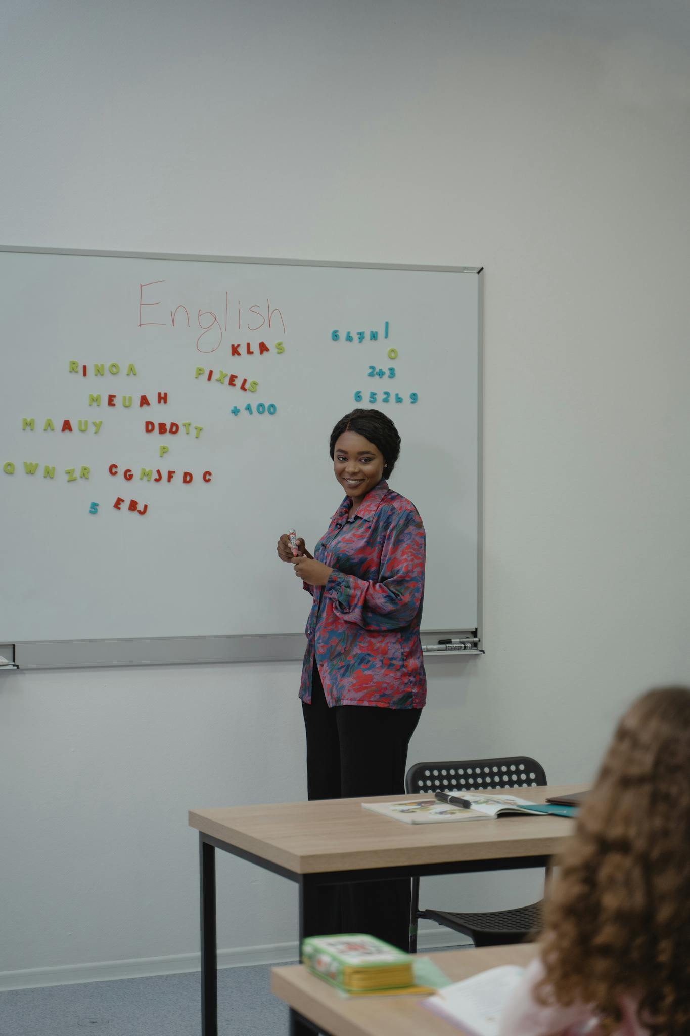 A female teacher explaining an English lesson to students in a classroom with a whiteboard.
