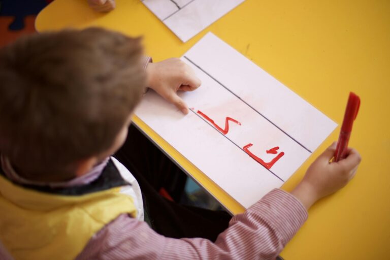 A young child practicing Arabic script writing at school on a bright yellow desk.